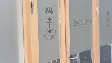 A room with a wooden door and a glass wall. The wall has a logo with a crown and anchor, and the word "FREGATTEN" is visible.