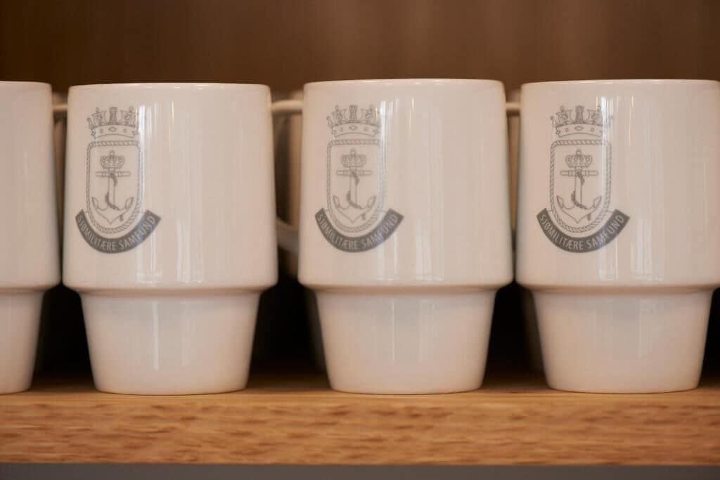 A row of white ceramic mugs with embossed logos, arranged on a shelf.