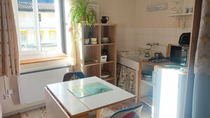 A small kitchen with a table and chair, a potted plant, and a window with curtains.