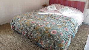 A bedroom with a floral bedspread, a red headboard, and wall-mounted lamps.