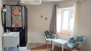 A bedroom with a bed, a desk, a chair, a small table, a sink, and a window.