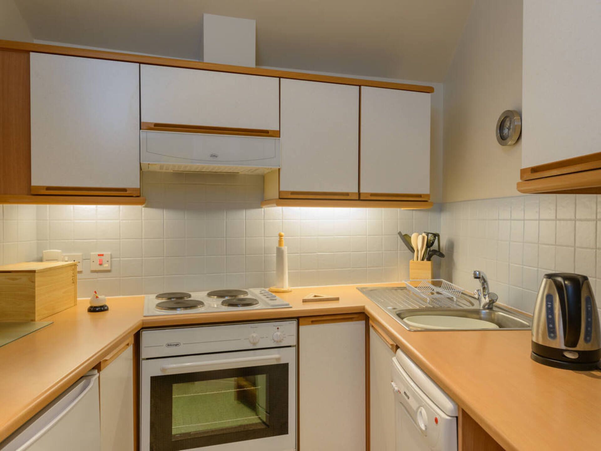 Une cuisine de taille réduite avec des meubles blancs, une cuisinière, un four, un lave-vaisselle et un évier.