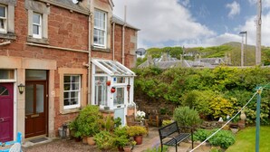 A stone house with a conservatory, a garden with potted plants, and a bench. - Dunlin - 1 Bedroom Seaside Apartment (North Berwick)