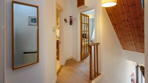 A hallway with a wooden staircase, a door with a mirror, and a ceiling light fixture. - Dunlin - 1 Bedroom Seaside Apartment (North Berwick)