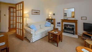 A cozy living room with a checkered sofa, a wooden coffee table, a fireplace, and a television. - Dunlin - 1 Bedroom Seaside Apartment (North Berwick)