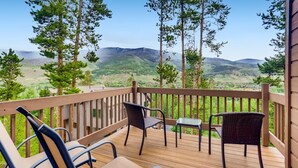 Une terrasse en bois, agrémentée de chaises et d’une table en osier, qui offre une vue sur un paysage montagneux.