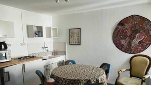 Una cocina compacta con comedor, que incluye una mesa redonda con mantel colorido, dos sillas y un adorno en la pared.