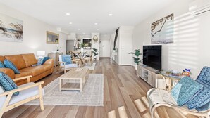 Uma sala de estar moderna com um sofá de couro marrom, uma televisão e um espaço de jantar com móveis de madeira.