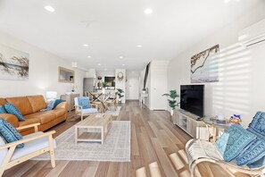 Een moderne woonkamer met een bruine leren bank, een televisie en een eethoek met houten meubels.