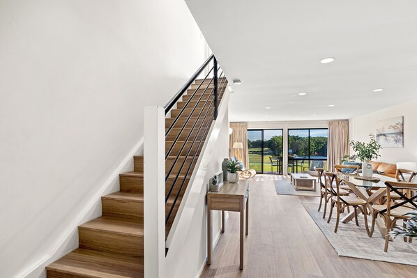 A spacious living area with a staircase, a dining table, and a view of the outdoors.