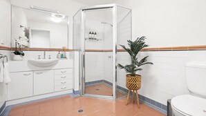 Um banheiro moderno com box de vidro, pia branca e planta em vaso.