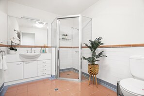 Een moderne badkamer met een douchecabine van glas, een wit wastafelmeubel en een potplant.