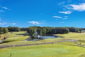 A golf course with a pond, trees, and a clear sky.