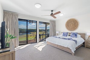 Ein Schlafzimmer mit einem großen Bett, einem Deckenventilator, Blick auf eine grüne Landschaft durch die Glasdoor und einer gewebten Wanddekoration.