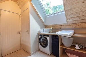 A compact laundry room with a washing machine, a drying rack, and a skylight.