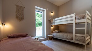 Una camera da letto con un letto singolo, un letto a castello, un piccolo tavolino rotondo e un pannello decorativo in macramè.