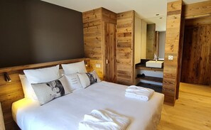 Une chambre moderne avec un grand lit, un lambris en bois, une armoire intégrée et une salle de bain avec un miroir et un lavabo.
