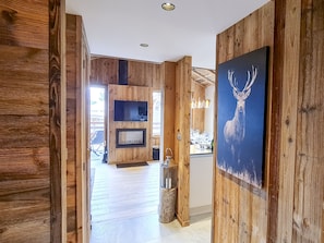 Un couloir intérieur en bois mène à une salle à manger où sont installés un téléviseur et un tableau représentant un cerf.
