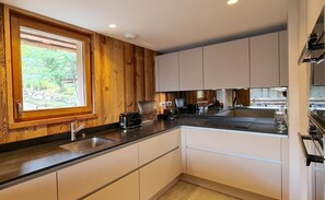 Une cuisine moderne avec un lambris en bois, des armoires blanches, une grande fenêtre et une cuisinière encastrée.