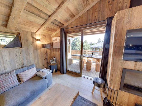 Un interior de madera con un sofá, un taburete pequeño, una mesa y un puerta corrediza de vidrio que da a una terraza exterior.