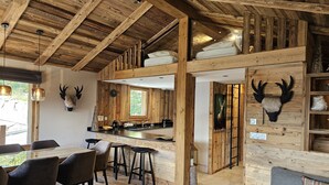 Ein rustikales Interieur mit Holzbalken, einer Küchenzeile und einer Sitzecke mit Sofa und Sesseln.