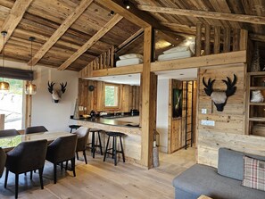 Een rustiek interieur met houten balken, een keukenhoek en een zithoek met een bank en stoelen.