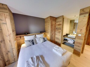 A modern bedroom with a large bed, wooden headboard, a built-in wardrobe, and a bathroom with a mirror and sink.