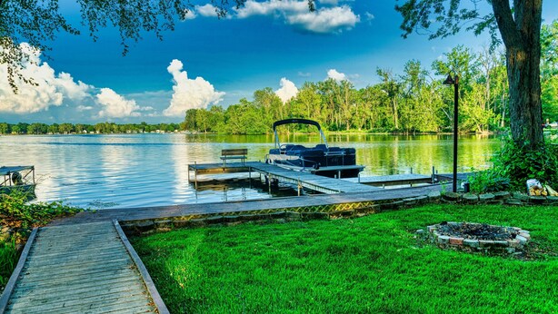 A dock with a boat, a grassy area, and a lake with trees in the background. - "Pier"adise on Long Lake - Lakefront Home (Portage)