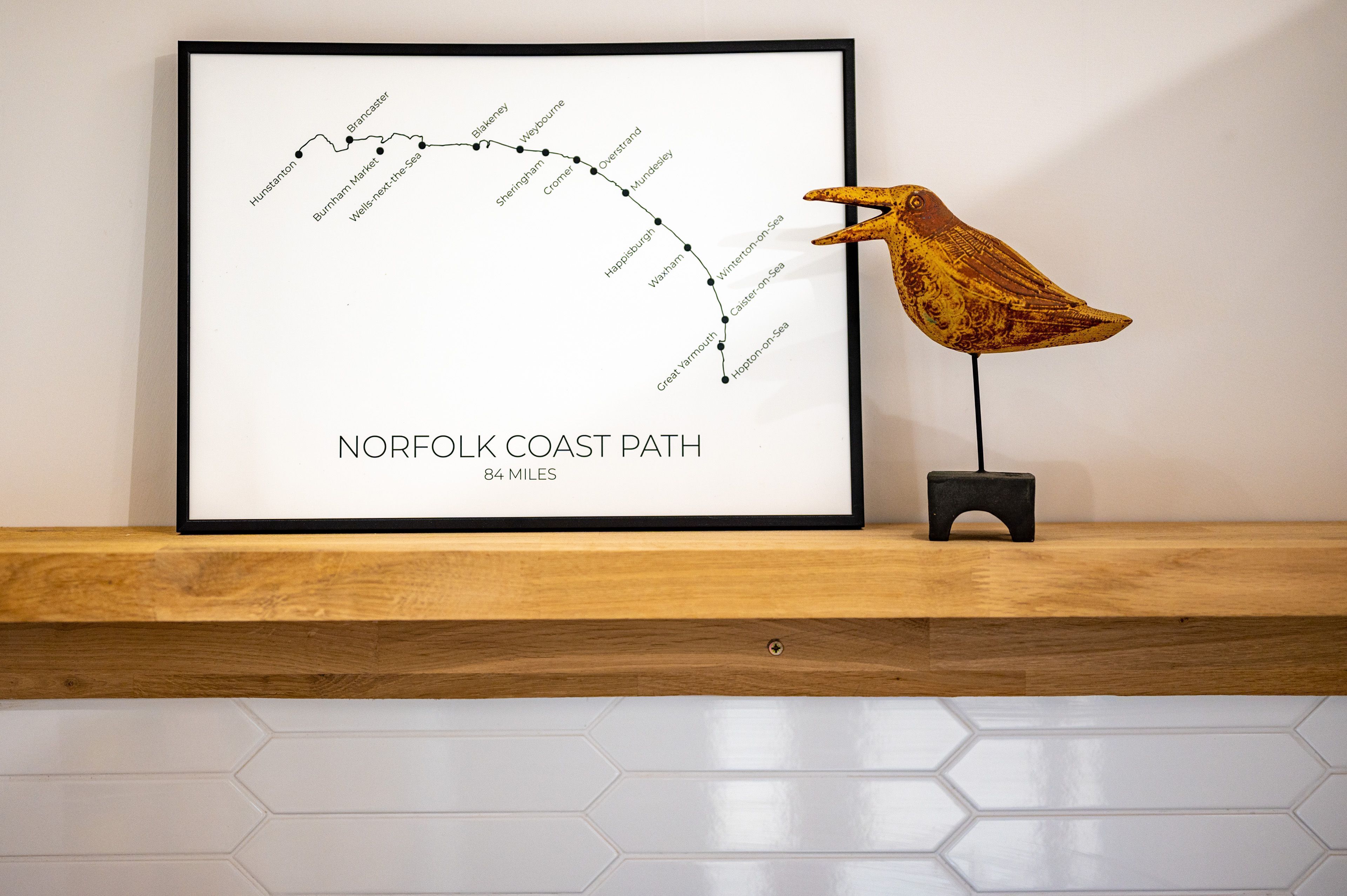 A framed map of the Norfolk Coast Path with a decorative bird sculpture on a shelf.