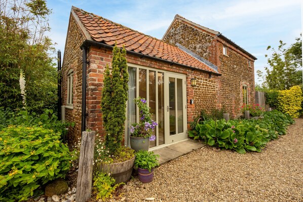 A brick house with a tiled roof, a large window, and a door with glass panels. - The Smokehouse, Ingoldisthorpe, Norfolk (Ingoldisthorpe)