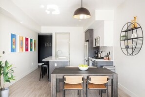 A modern kitchen with a dining area, featuring a wooden table, chairs, and a hanging light fixture. - Art-Inspired Loft | Mountain View | Zuni Lofts (Denver)