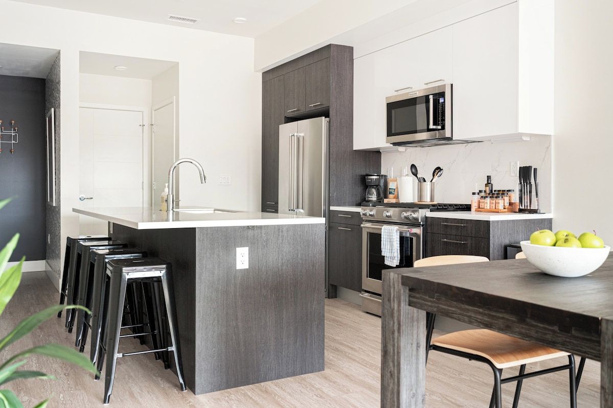 A modern kitchen with a central island, bar stools, a microwave, and a coffee maker.