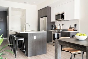 A modern kitchen with a central island, bar stools, a microwave, and a coffee maker. - Art-Inspired Loft | Mountain View | Zuni Lofts (Denver)
