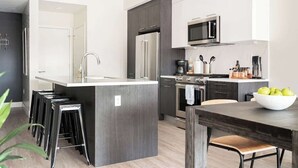 A modern kitchen with a central island, bar stools, a microwave, and a coffee maker. - Art-Inspired Loft | Mountain View | Zuni Lofts (Denver)