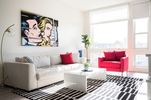 A living room with a sofa, a red armchair, a coffee table, and a large window.