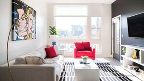A modern living room with a sofa, red armchair, and a coffee table. There is a large window providing a view of the city. - Art-Inspired Loft | Mountain View | Zuni Lofts (Denver)