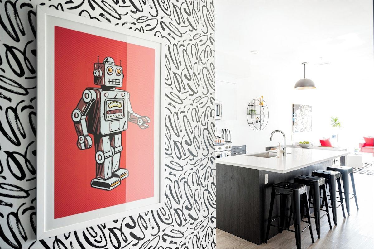 Cuina moderna amb una illa central, tamboretes de bar i una obra d'art emmarcada d'un robot.