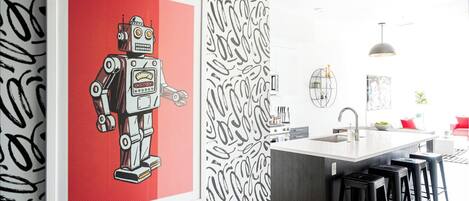 Een moderne keuken met een centraal eiland, barkrukken en een lijstwerk met een afbeelding van een robot.