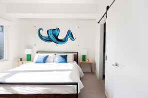 Une chambre à coucher comprenant un lit, deux tables de chevet, une œuvre d’art accrochée au mur et une porte.