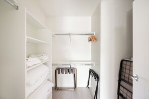 A room with white walls, a bed with white linens, a metal rack with clothes, and a radiator. - Art-Inspired Loft | Mountain View | Zuni Lofts (Denver)