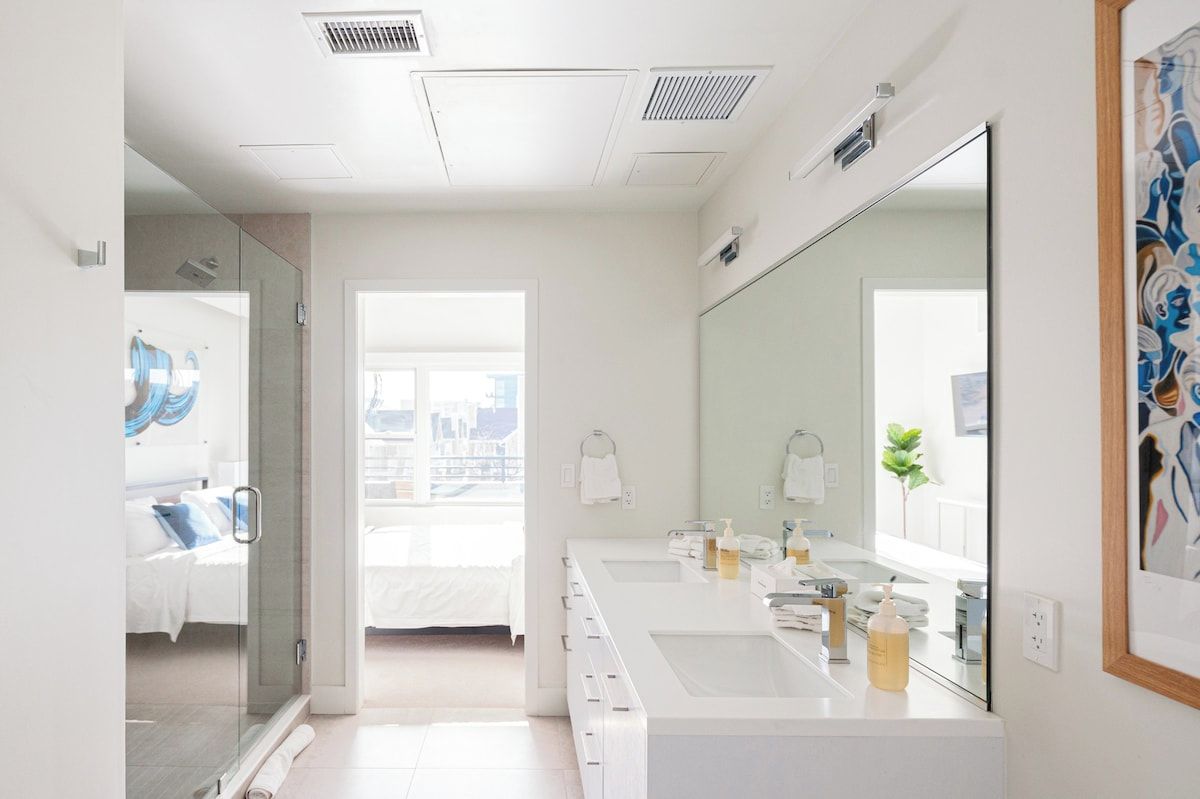 Une salle de bain moderne avec un grand miroir, deux lavabos et un espace douche.