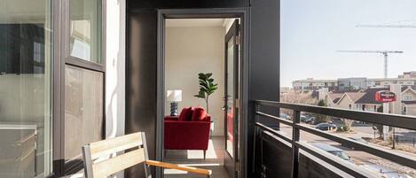 A balcony with a wooden bench, a red sofa, and a potted plant.