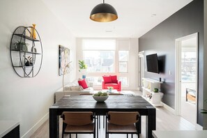 A modern living room with a dining area, a large window, and a flat-screen TV mounted on the wall. - Art-Inspired Loft | Mountain View | Zuni Lofts (Denver)