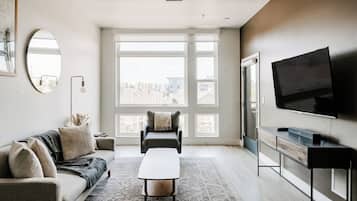 A modern living room with a sofa, a coffee table, a TV, and large windows.