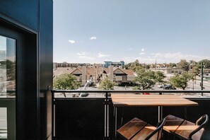 A balcony with a view of a residential area, a wooden table, and chairs. - Contemporary Cool Lifestyle Loft | Zuni Lofts (Denver)