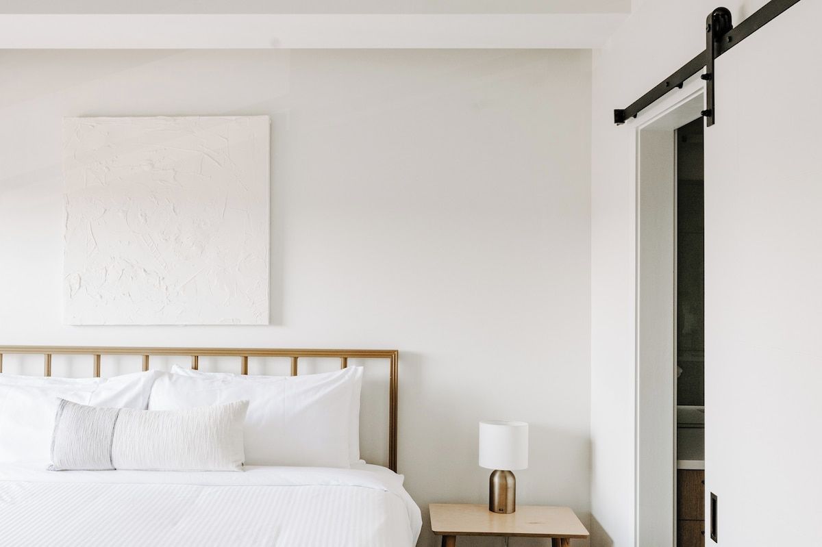 A hotel room with a bed, a bedside table with a lamp, a wall-mounted artwork, and a sliding door.