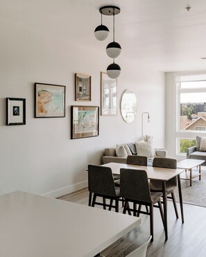 A modern living room with a dining area, featuring a sofa, chairs, a coffee table, and artwork on the walls.