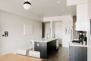 A modern kitchen with a central island, white cabinetry, and a stainless steel range hood. - Contemporary Cool Lifestyle Loft | Zuni Lofts (Denver)