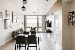 A modern living room with a sofa, dining table, chairs, a TV, and artwork on the walls.
