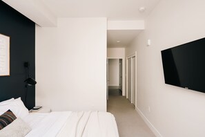 A modern bedroom with a bed, a mounted TV, and a hallway leading to another room.